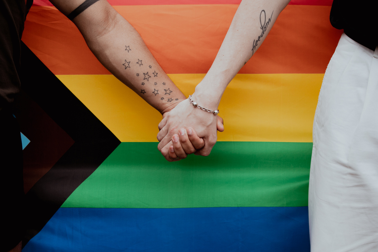 Two People Holding Hands by a Progress Pride Flag