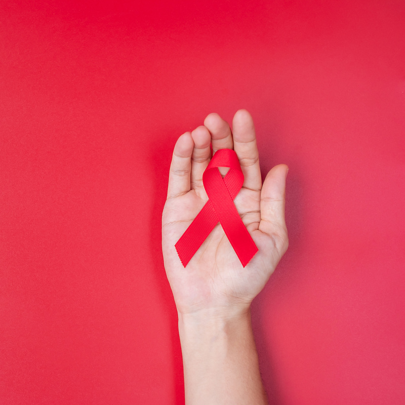 Hand holding Red Ribbon for supporting people living and illness. Healthcare and safe sex concept. December World Aids Day and multiple myeloma Cancer Awareness month